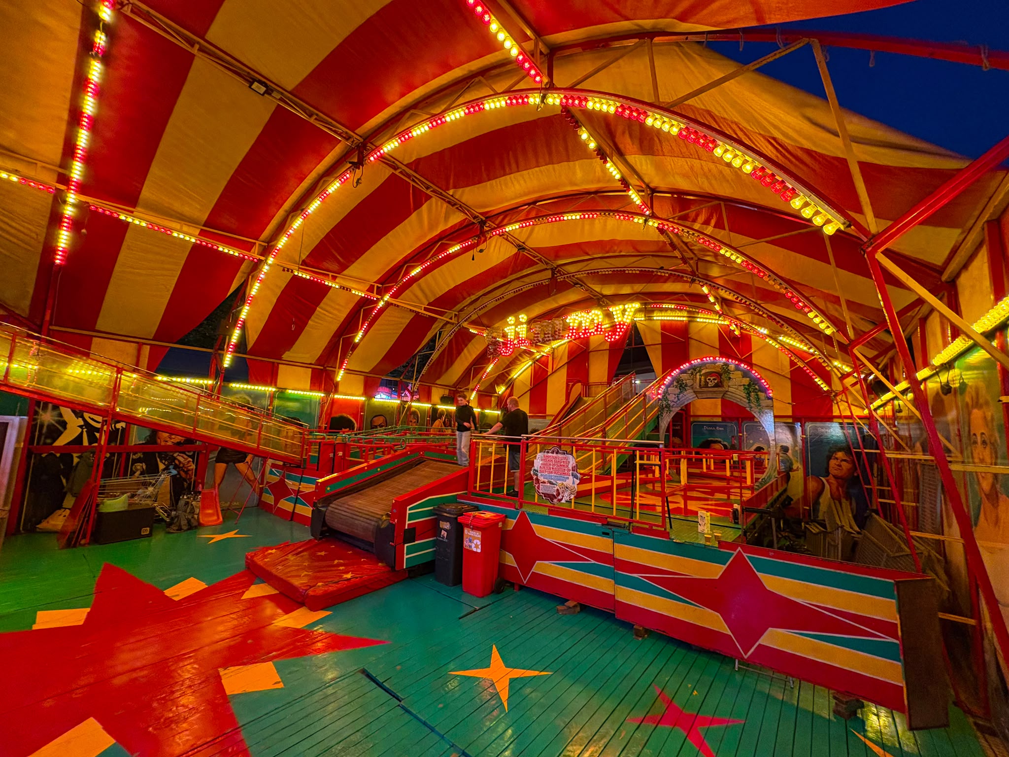 Cakewalk Cakewalk-attractie Sjimmy in de avond, met verlichte tentboog en zicht op de glijbaan en wandelbaan