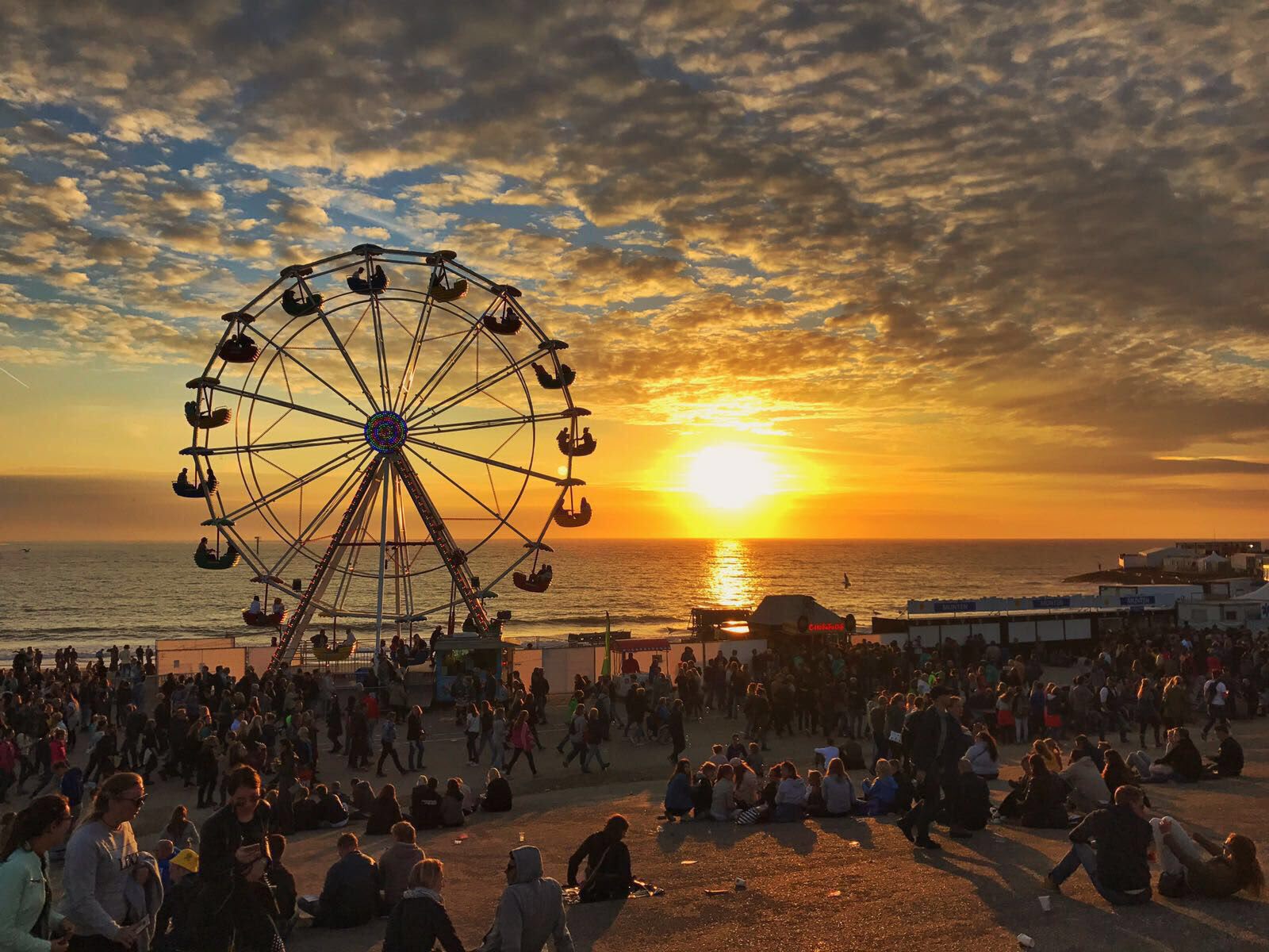 Reuzenrad Nostalgisch reuzenrad met gondels bij zonsondergang aan het strand, met publiek op het evenemententerrein